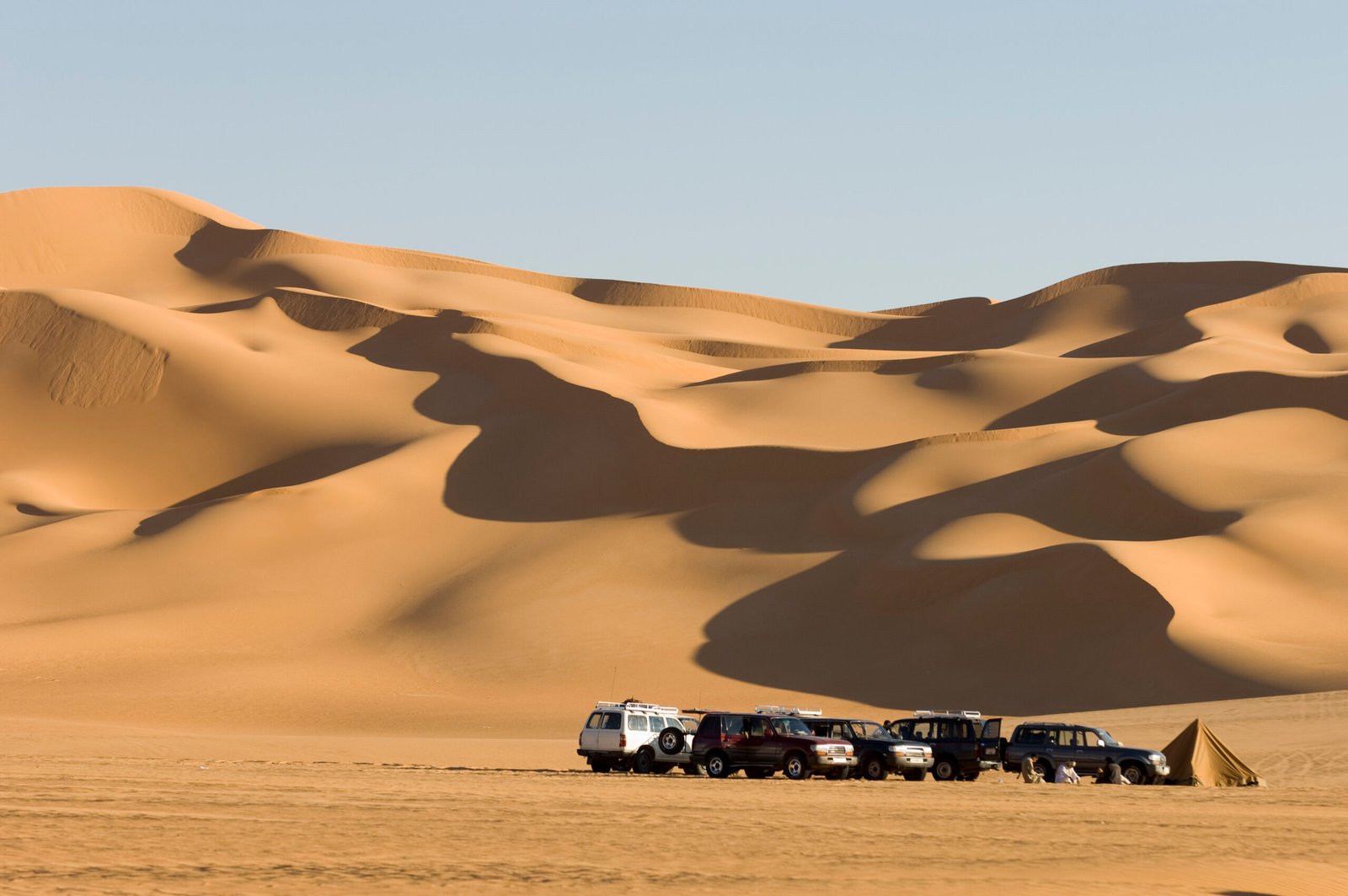 Caravan of offroad vehicles at rest in the expansive desert dunes.