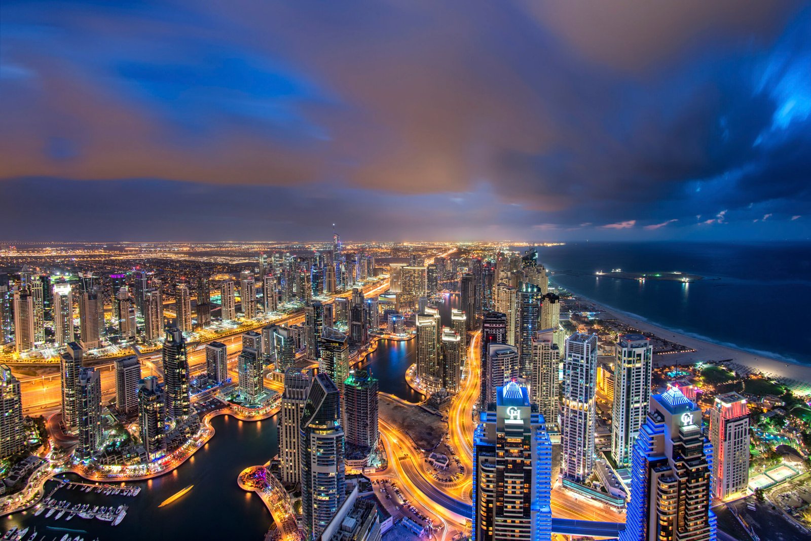 Cityscape of the Dubai, United Arab Emirates at dusk, with illuminated skyscrapers and coastline of the Persian Gulf.